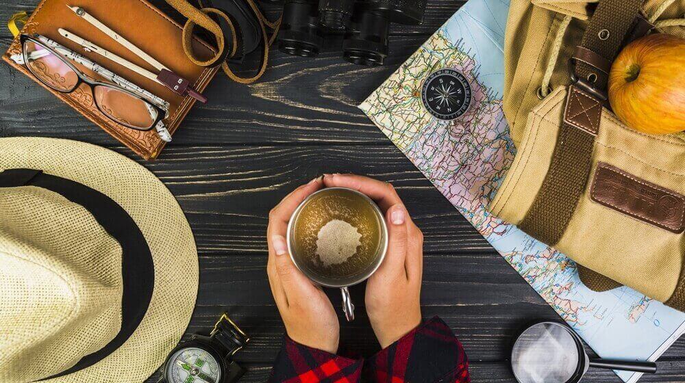 traveler hand holding cup coffee surrounded with various travelling equipments