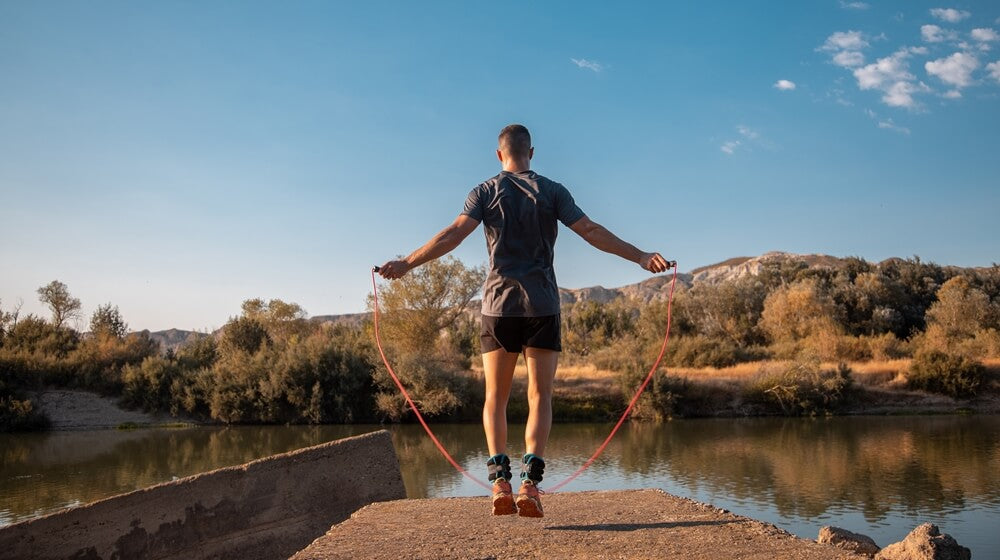 man exercising while traveling with jumping rope river